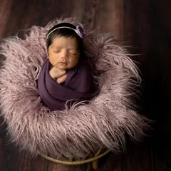 Simplicity at its best. This newborn is wrapped in a deep purple swaddle and resting in a soft, fluffy basket. The dark wood background makes the colors pop.
