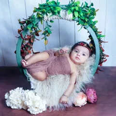 An awake baby girl looking calmly towards the camera while posed in a beautiful green floral hoop. Her calm demeanor makes for a stunning portrait.