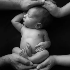 A creative and symbolic pose, with the parents' and sibling's hands forming a protective circle around the newborn.