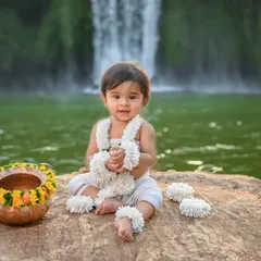 An outdoor shoot with a traditional touch. This baby is sitting by a serene waterfall, creating a beautiful contrast between the natural environment and the simple, traditional attire.