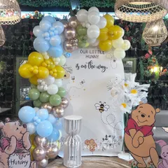 This is our 'A Little Hunny is on the Way' baby shower theme, inspired by Winnie the Pooh. The setup features a custom arched backdrop, character standees of Pooh and Piglet, and a unique balloon arch with a mix of pastel and honey-colored balloons to create a warm, gentle atmosphere.