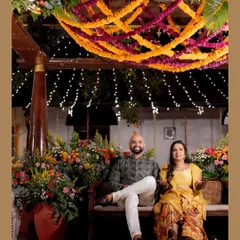 A magical Mehendi night comes to life with vibrant marigold garlands crisscrossing the ceiling, dotted with fairy lights. The seating area is surrounded by lush, colorful floral arrangements, creating a warm and festive atmosphere.