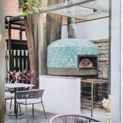 As featured in a magazine, this shot shows the beautiful mosaic-tiled pizza oven at Kana Cafe, perfectly integrated with the outdoor seating area and surrounding nature.