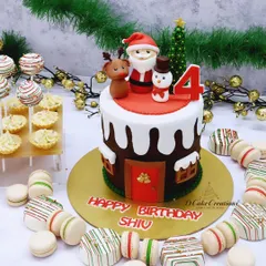 A fun and festive Christmas-themed birthday cake for a December baby. This design features a Santa's workshop theme with edible figures of Santa, a reindeer, and a snowman, complemented by holiday-themed macarons and cake pops.