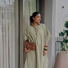 A candid shot showing the wooden clutch as part of a relaxed, elegant outfit. The natural wood tones are a perfect complement to the earthy green of the dress.