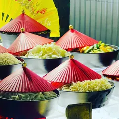 This live station features a variety of ingredients for a build-your-own Chinese bowl. The setup is adorned with traditional red paper hats and fans, adding a touch of authenticity and visual flair to the experience.