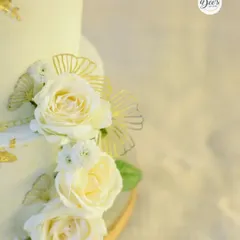 A close-up view reveals the texture of the buttercream and the delicate details of the fresh flowers and gold accents on this wedding cake.