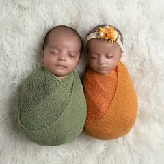 A sweet shot of newborn twins, swaddled in complementary colors, nestled together on a soft white rug.