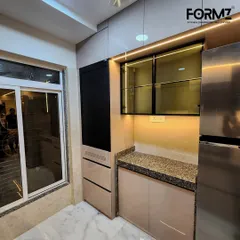 A full view of the storage and appliance wall in this kitchen. The design neatly integrates the refrigerator, a roller shutter unit, and display cabinets, ensuring a cohesive and organized look.