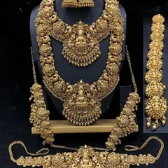 This is a full antique-finish temple jewellery set, perfect for achieving a classic bridal look. The set includes a choker, a long haaram, matching jhumkas, a vaddanam (waist belt), and hair accessories, all featuring intricate deity and peacock motifs.