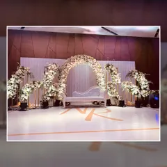 This elegant reception stage features a beautiful arch of white flowers over a classic white chaise lounge. The custom monogram of the couple on the floor adds a lovely personal touch to the sophisticated design.