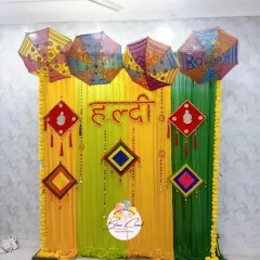 A vibrant Haldi ceremony backdrop with yellow and green drapes, decorated with colorful umbrellas and traditional hangings.