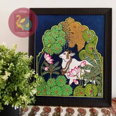Here is the framed Pichwai Cow painting, ready to bring a sense of peace and pastoral beauty to a home. The contrast between the dark background and the vibrant greens and pinks makes it a truly eye-catching piece.