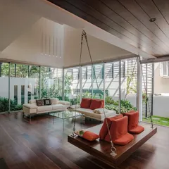 A family space in the Sandeep & Neelam Residence, designed for seamless indoor-outdoor living. The floor-to-ceiling glass walls dissolve the boundary to the garden, while the indoor swing adds a playful element to the minimalist design.