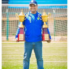 A proud coach holding two championship trophies on the field. This is the result of the hard work we put into every tournament.