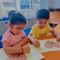 Two children work side-by-side on a "Love You" card, practicing their fine motor skills and learning to express emotions through art and words.