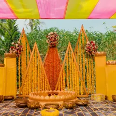 A geometric and colorful Haldi stage. We used triangular wooden frames decorated with marigold strings to create a modern yet traditional backdrop, complemented by brass bowls and a lotus seat for the bride or groom.
