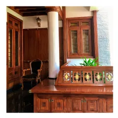 This elegant sit-out space, or verandah, showcases the beauty of traditional woodwork. The polished wood, classic furniture, and detailed joinery create a serene space for relaxation, typical of a Kerala veedu.