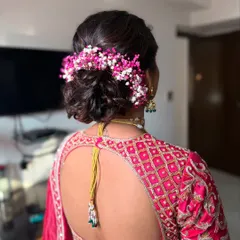 A detailed look at a textured bridal bun, intricately woven and adorned with colorful pink and white baby's breath. This style is perfect for coordinating with pastel or pink-toned outfits.