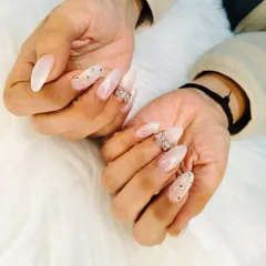 An angelic set of long, almond-shaped extensions with a milky white base, adorned with sparkling rhinestone bows and scattered gems.