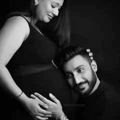 An intimate black and white maternity portrait showing an expecting father listening to the baby bump. This studio shot uses classic lighting to emphasize the emotional connection and anticipation of the couple.