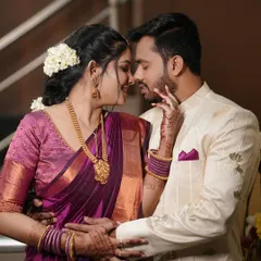 A beautiful, intimate moment between an engaged couple. Her makeup is classic and elegant, with a focus on defined eyes and a glowing complexion that complements her purple silk saree.