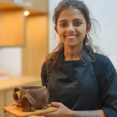 A student proudly displays her finished house-shaped mug, complete with intricate details like a textured roof and a twisted handle. Hand-building allows for endless creativity and personalization.
