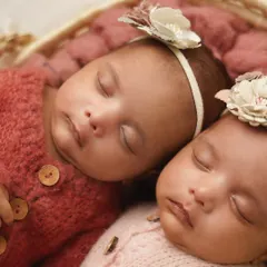 A close-up of the twin girls, dressed in adorable matching knit rompers in different colors. Their closeness in the photo emphasizes their special bond.