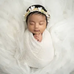 Simplicity at its best. A baby swaddled in white on a bed of soft, white tulle fabric. The floral headband adds a delicate touch to this angelic portrait.