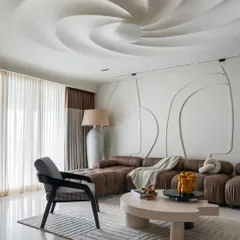 In this residential living room, the ceiling becomes a sculptural centerpiece. The swirling form creates a sense of movement and draws the eye upward, transforming a flat surface into a dynamic work of art. This feature, combined with the abstract wall molding, establishes a bold and eccentric personality for the home.