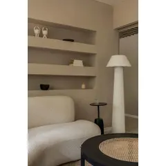 The client lounge is designed as a peaceful retreat, featuring a custom-designed curved sofa in a textured white fabric. Built-in wall niches provide space for subtle decor, while a tall, fluted floor lamp casts a soft, ambient glow.