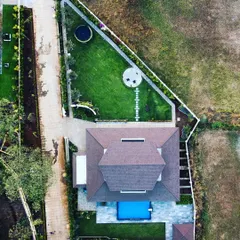 An overhead drone shot providing a clear view of our landscape layout for this villa. You can see the distinct zones we created: the poolside leisure area, the central lawn with a circular seating spot, and the tree-lined pathways, all designed for a seamless flow.