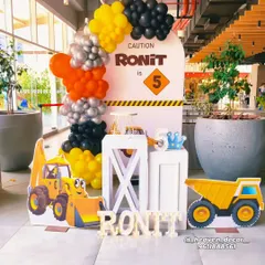 A fun and bright construction-themed 5th birthday party. This setup includes a custom "Caution" sign backdrop, character cutouts of a digger and dump truck, and a balloon garland in classic construction colors of yellow, black, and orange.