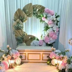 A beautiful and modern setup featuring a crescent-shaped arch made of pink and white flowers and dried palm leaves. This boho-inspired design is perfect for an elegant and contemporary celebration.