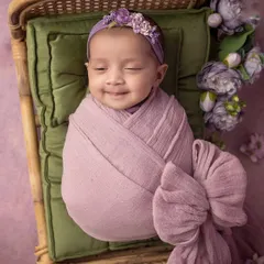 A smile as sweet as a flower. This newborn girl, wrapped in a beautiful lavender bow, is the picture of pure, sleepy joy.