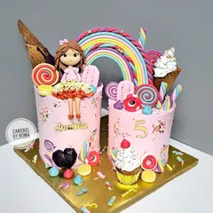 Welcome to Candyland. This vibrant pink cake duo is a sweet dream come true, decorated with lollipops, macarons, ice cream cones, and a custom doll topper made to look just like the birthday girl.