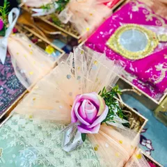 Beautifully decorated sagan favours for a wedding. Each gift box is wrapped in delicate peach and mint green net fabric with gold polka dots, and finished with a small rose and ribbon, creating a pretty and traditional party favour.