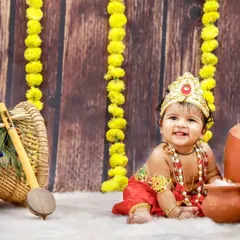 Celebrating Krishna Jayanthi with this adorable little Krishna. The setup includes clay pots, marigold garlands, and a peacock feather, creating a festive scene.