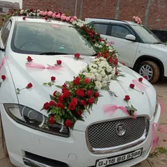 A beautiful floral design on a white Jaguar. The arrangement flows diagonally across the car, using red and white roses with delicate pink ribbons for an elegant touch.
