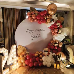 This is a beautiful birthday decoration I created for a celebration at home. It features a personalized circular backdrop with the birthday person's name, framed by a balloon arch in a sophisticated red, gold, and white color scheme. The illuminated '24' adds a special touch for a milestone birthday.