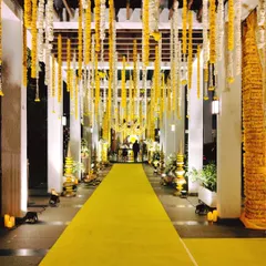 A grand pathway for a Sai Sandhya, lined with a vibrant yellow carpet and decorated with hanging garlands of marigolds. This long, dramatic entrance builds anticipation and creates a serene atmosphere.