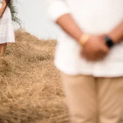 An artistic composition focusing on the bride-to-be standing in a field of dry grass, with her partner blurred in the foreground. This creative shot evokes a sense of anticipation and connection.