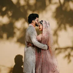 A silhouette of love. The groom gently kisses his bride's forehead against a sunlit wall, creating a timeless and artistic portrait.