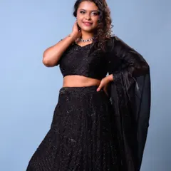 A full-length view of this gorgeous bridesmaid in a black lehenga. The makeup features a silver smokey eye and the hair is styled in tight, defined curls for a modern party look.