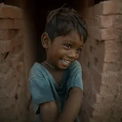 A candid portrait of a young boy at a brick kiln, his shy but genuine smile offering a moment of light and happiness in a harsh environment.
