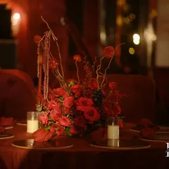 A stunning centerpiece combining red roses, dried branches, and grapes. The varied textures and shades of red add depth and sophistication to the arrangement.