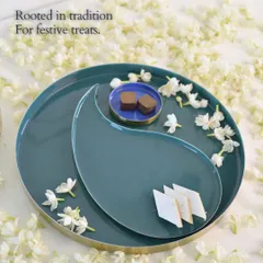 Rooted in tradition, for festive treats. The beautiful teal and blue serving platter, with its elegant paisley-inspired shape, is perfect for presenting traditional sweets like kaju katli and chocolate barfi, surrounded by fragrant jasmine flowers.