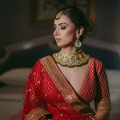 A bride in a moment of reflection, wearing a stunning gold-plated Kundan choker with green beads. This is one of our most popular single-piece rentals for brides.