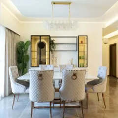 Luxury dining at its finest. This space from the Bren Zahara project features quilted high-back chairs, a stunning crystal chandelier, and a backlit crockery unit with metallic and glass details.