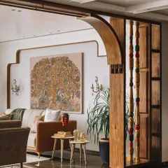 I love creating partitions that define a space without closing it off. Here, a wooden arch with colorful Channapatna pillars separates the living area, adding an element of traditional craft. The design allows for a clear view of the custom Kalamkari art, blending art and architecture seamlessly.